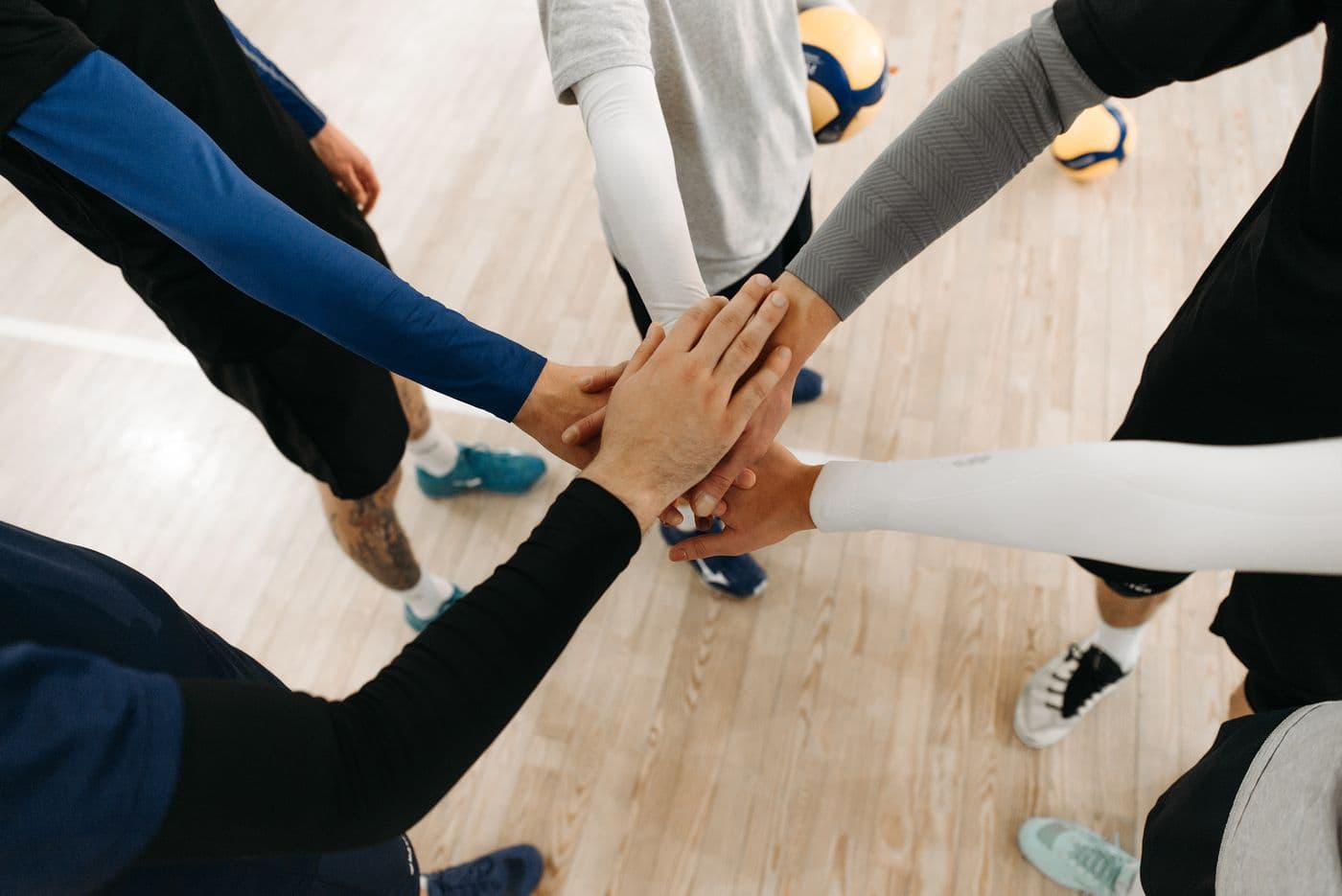 A team in sportswear standing in a circle on an indoor court with their hands stacked together in the middle.